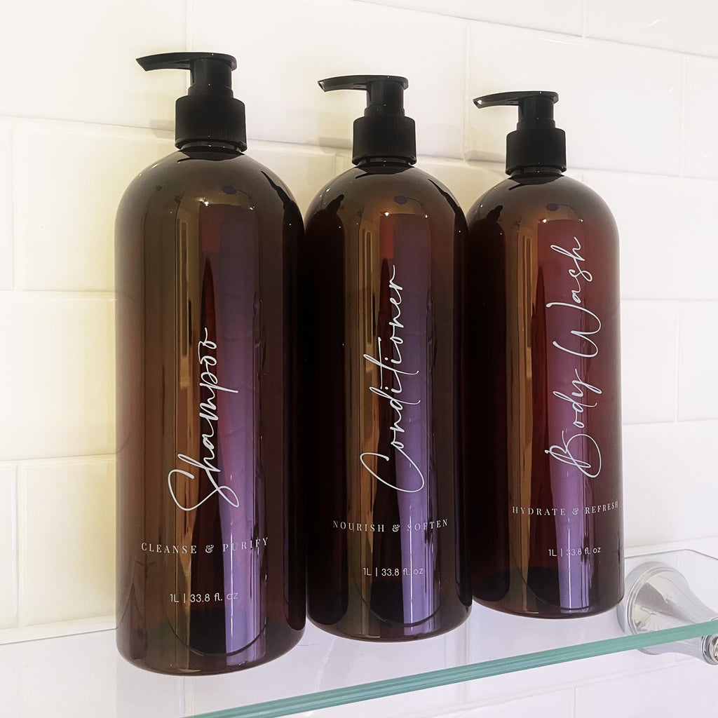 Three brown refillable pump bottles labelled 'Shampoo', 'Conditioner', and 'Body Wash'. Elegant, minimalist design bathroom decor and shower organisation.